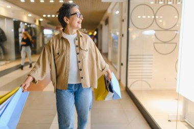 Parlak bir alışveriş merkezinde yürürken gülümseyen son sınıf öğrencisi bir kadın.