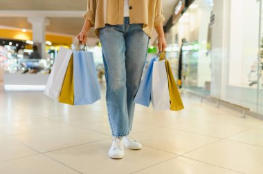 Kadının alttaki bedeni, alışveriş merkezinin koridorunda yürürken görüldü. Satış çılgınlığından kalma bir sürü çanta taşıyordu.