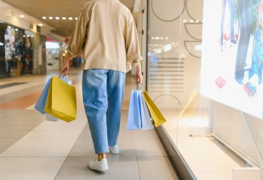 Tüketiciler renkli perakende çantalar taşırken, aydınlık, modern bir alışveriş merkezinde yürürken, tüketiciliğin ve yaşam tarzının keyfini çıkarıyorlar.