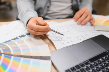 İç mimar yeni bir proje için renk ve bitiş çizimleri seçiyor, masa üzerinde planlar, renk paleti ve dizüstü bilgisayarla çalışıyor