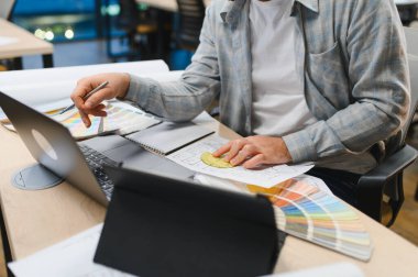 Yer planları ve renk örnekleri olan bir dizüstü bilgisayarda çalışan iç mimar, müşteriler için yeni tasarım kavramları geliştiriyor