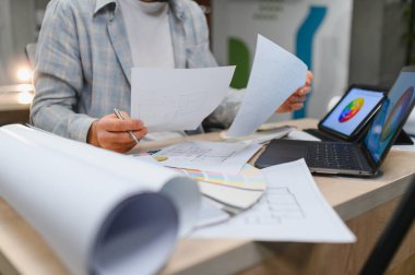 Masada çalışan iç mimar, planları ve planları gözden geçiriyor. Dizüstü bilgisayar ve tablet renk çarkı ve kavramları gösteriyor