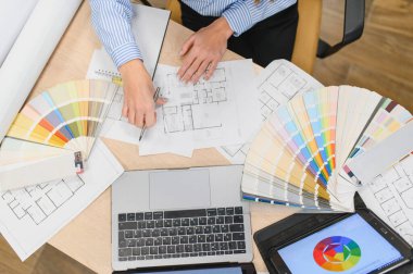 Tasarımcı elleri planlar ve kat planları üzerinde çalışıyor, kumaş kumaş kitapları ve ev yenileme için dijital araçlarla renkler seçiyor