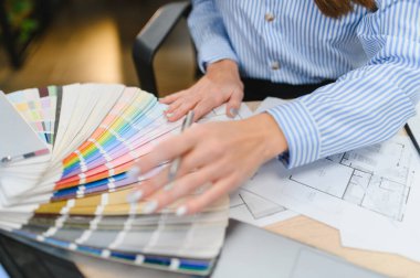Profesyonel eller bir kumaş parçasından renkler seçiyor, iç tasarım için bir plan ve mimari kat planı üzerinde çalışıyor.