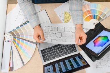 Profesyonel eller bir plan tutuyor. Renk örnekleri, dizüstü bilgisayarlar ve tabletlerle bir iç tasarım projesi hazırlıyorlar.
