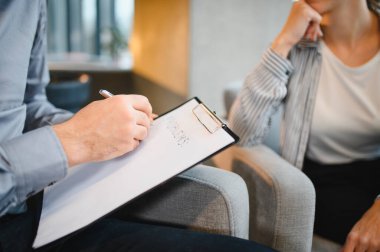 Profesyonel psikoterapist, hayal kırıklığına uğramış bir kadınla zihinsel sağlık danışmanlığı sırasında panoya notlar yazıyor.