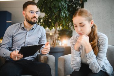 Terapi seansında üzgün bir genç kadını dinleyen psikolog zihinsel sağlık desteği ve duygusal refahına odaklanıyor.