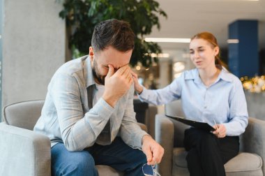 Şefkatli bir kadın psikologla terapi seansı sırasında yüzünü duygusal çöküntüye sokup destek veren ve dinleyen bir adam.