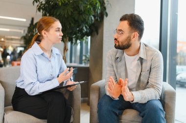 Genç bir adam psikoterapi görüyor, seans sırasında bir kadın danışmanla konuşuyor, akıl sağlığına hitap ediyor.
