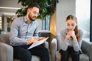Koltukta oturan genç bir kadın, psikoloğunun akıl sağlığını tartışmasını dinliyor ve ona destek oluyor.