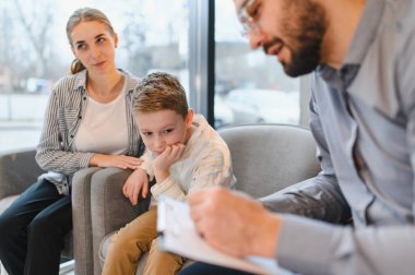 Terapi seansı sırasında annesiyle oturan genç bir çocuk, bir erkek psikologdan profesyonel yardım alıyor.