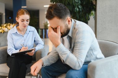 Üzgün bir adam terapi sırasında şefkatli bir kadın terapistle duyguları tartışıyor, duygusal destek ve yardım arıyor.