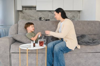 Sevgi dolu anne hasta oğluna ilaç veriyor. Kanepede dinleniyor. İyileşme sürecinde ona bakıyor.