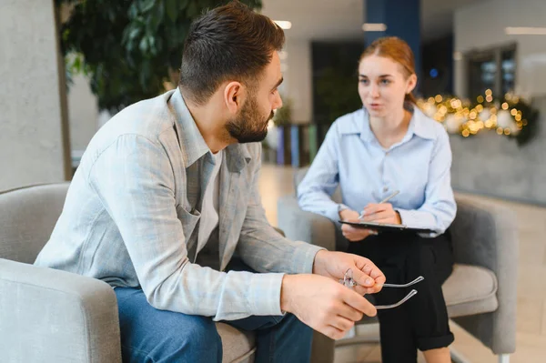 Genç adam kadın psikologla görüşüyor. Sandalyelerde oturuyor ve konuşuyor. Zihinsel sağlık ve terapiye odaklanıyor.