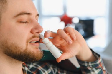 Burun spreyi kullanan genç bir adam nezle, grip ya da mevsimsel alerji semptomlarını kontrol ediyor. Tıkanıklıktan kurtulmak