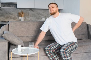 Sırtını tutan, yaralanma ya da hastalıktan rahatsızlık duyan, ilaç ve suyun yanında oturan bir adam.