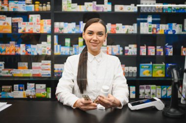 Tezgahın arkasında beyaz önlüklü gülümseyen eczacı elinde ilaç ve haplarla profesyonel sağlık hizmetleri sunuyor.
