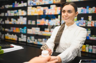 Genç bir kadın eczacı modern bir eczanedeki müşteriye ilaç ve su toplayıcı paketi veriyor.