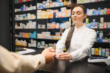 Eczacı tezgahın arkasında durup eczanedeki müşteriye bir şişe ilaç ve su topladı.