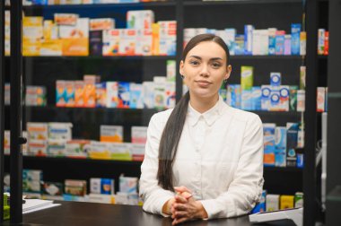 Modern bir eczanede çalışan genç bir kadın eczacı müşterilere profesyonel sağlık danışmanlığı ve tıbbi yardım sunuyor.