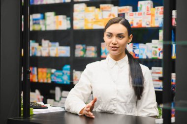 Laboratuvar önlüğü giyen kadın eczacı, modern bir eczanenin tezgahında durup hastanın ilaç dağıtmasına yardım ediyor.