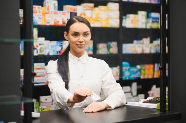 Eczane tezgahında çalışan dost canlısı bir kadın eczacı. Bir paket hap veriyor, profesyonel sağlık hizmeti sunuyor.