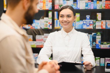 Gülümseyen eczacı, modern eczane tezgahında çalışan bir erkeğe dostça danışmanlık ve ilaç hizmeti sunuyor.