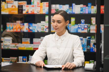 Eczane tezgahında çalışan kadın eczacı, modern bir eczanede sağlık, tıp ve profesyonel bakımı yansıtıyor.