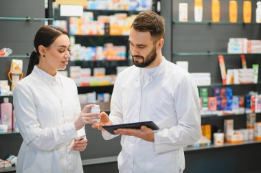 Modern bir eczane ortamında dijital bir tabletle reçete ve uyuşturucu detaylarını tartışıp işbirliği yapan eczacılar