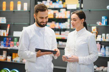 Dijital tablete bakan eczacılar modern bir eczanede reçeteli ilaçları tartışıyor ve sağlık hizmetleri danışmanlığı sağlıyorlar.