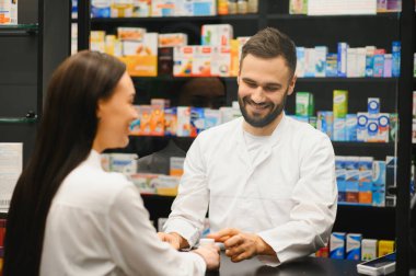 Bir kadın müşteriye ilaç verirken gülümseyen eczacı, modern bir eczanede profesyonel sağlık hizmeti sunuyor.