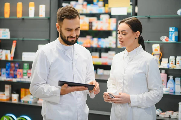 Dijital tablete bakan eczacılar modern bir eczanede reçeteli ilaçları tartışıyor ve sağlık hizmetleri danışmanlığı sağlıyorlar.