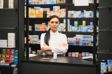 Tezgahın arkasında duran genç kadın eczacı müşterilerine sağlık hizmeti verdiğinden emin.