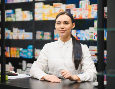 Modern bir perakende eczanesinde çalışan profesyonel kadın eczacı, sağlık hizmeti ve ilaç bilgileri sunuyor