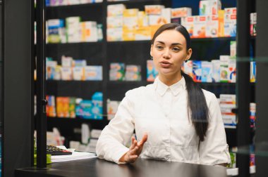 Beyaz önlüklü genç bir kadın eczacı eczanedeki müşterilerine profesyonel tavsiyelerde bulunuyor.