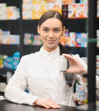 Elinde ilaç şişesi olan beyaz üniformalı profesyonel bir kadın eczacı eczanede sağlık ve ilaç hizmeti sunuyor.