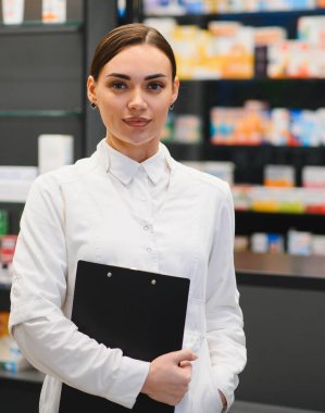 Beyaz önlüklü genç bir kadın eczanede sağlık uzmanı olarak çalışıyor, tıbbi danışmanlık ve yardım öneriyor.