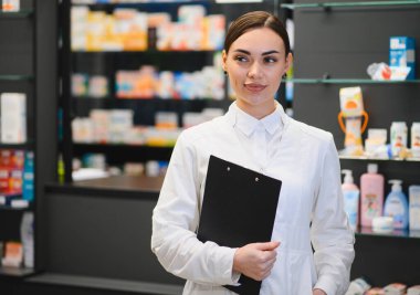 İlaç dolu rafların önünde duran genç bir kadın eczacı, elinde sağlık sigortası kutusunda bir pano tutuyor.
