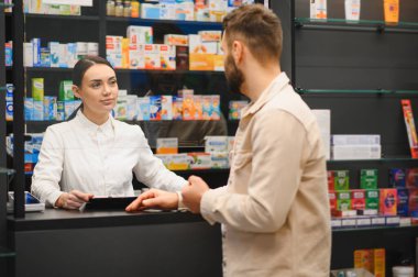 Modern bir eczanede erkek müşteriye yardım eden kadın eczacı, sağlık ve sağlık ürünlerini tartışıyor.