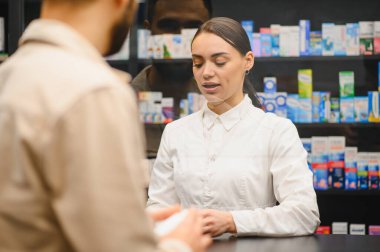 Kadın eczacı, modern bir eczanede ilaç tedavisi için erkek bir müşteriye danışıyor. Sağlık hizmetleri