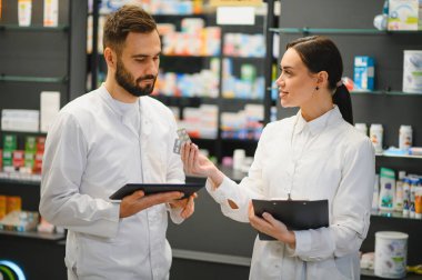 İki eczacı, bir erkek ve bir kadın, modern bir eczanede çalışırken ilaçları tartışıyorlar, profesyonel sağlık hizmeti sağlıyorlar.