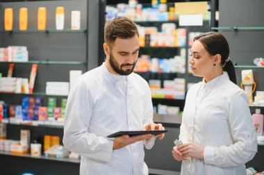 Eczacı ekibi, modern bir eczanede sağlık çözümlerini tartışıyor ve dijital bir tablet ve ilaçla envanteri yönetiyor.