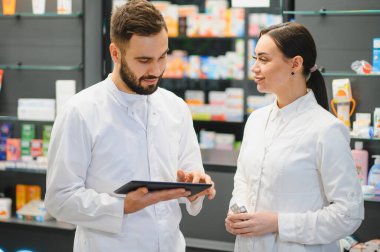 İlaçları tartışan eczacılar ve modern bir eczane ortamında sağlık yönetimi için dijital tablet kullanıyorlar
