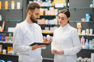 Eczanede işbirliği yapan eczacılar, dijital tabletteki ilaç detaylarını gözden geçirip ilaç paketlerini tutuyorlar.