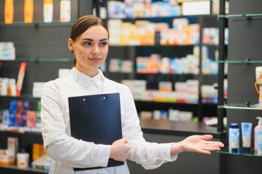 Genç bir kadın eczacı, pano danışmanlığı ile modern bir eczanede ilaç rafları ile sağlık hizmeti sunuyor.