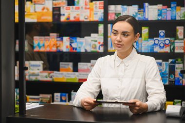 Tezgahta profesyonel hizmet sunan genç kadın eczacı. Etrafı ilaç ve sağlık ürünleriyle çevrili.