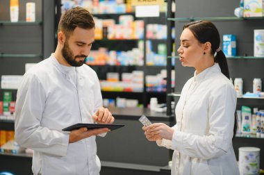 Modern bir eczanede ilaçları tartışan eczacılar, müşteri yardımı için dijital tablet hakkında araştırma yapıyorlar.