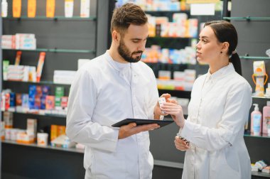 Dijital tablet kullanan eczacılar ve ellerinde su toplayan bir paket, sağlık ürünleri ve müşteri hizmetleri hakkında danışmanlık yapıyorlar.