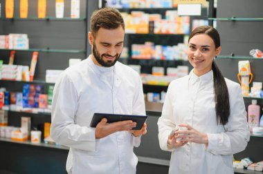 Eczacı ekibi dijital tablet hakkında danışmanlık yapıyor ve ilaç hazırlıyor, çağdaş bir eczanede duruyor.