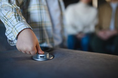 Çocuğun eli bir güç düğmesine basıyor ve modern bir kanepede bir USB portuna erişiyor. Ev teknolojisini ve rahatlığını simgeliyor.